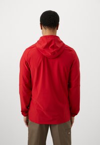 Giacca rossa con cappuccio, caratterizzata da una texture liscia e maniche lunghe, con una vestibilità su misura e cappuccio regolabile. La vista posteriore mostra un design semplice.