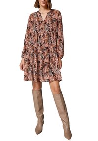 Robe à imprimé floral avec manches longues, décolleté en V et jupe à volants en orange, noir et blanc. Des bottes beiges jusqu'aux genoux complètent le look.