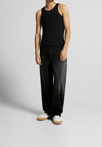 Svart bomullstopp i tankmodell tillsammans med lösa, mörk denimjeans och vita sneakers med gummisålar. Kroppen är något vänd åt sidan.