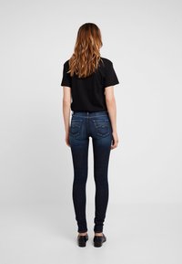 Jeans ajustados de denim oscuro, con un diseño de cinco bolsillos y acentos de costura, combinados con una camiseta negra básica y calzado negro.