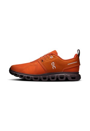 Chaussure de running orange avec semelle noire segmentée, laçage à l'avant, logo de la marque blanc et languette au talon sur fond blanc.