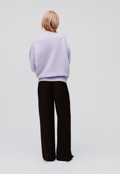 Lila oversized trui met verlaagde schouders, gecombineerd met zwarte wijde broekspijpen. Soepele textuur, minimalistisch ontwerp, effen achtergrond.