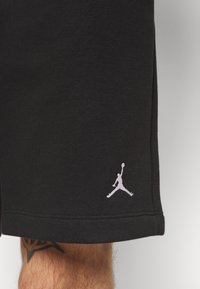 Black cotton shorts with a smooth texture, featuring a white Jumpman logo on the hem and stitched detailing.