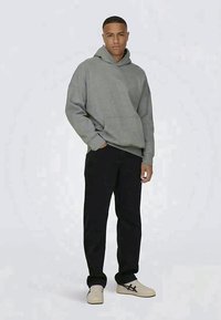 Sudadera gris de gran tamaño con un bolsillo canguro, combinada con pantalones negros y zapatillas ligeras. Textura suave y diseño relajado.