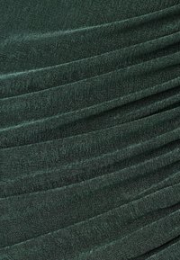 Dunkelgrüner Stoff mit einer strukturierten Webart, der diagonale Falten und einen dezenten Glanz aufweist. Das Material wirkt weich und fällt geschmeidig.