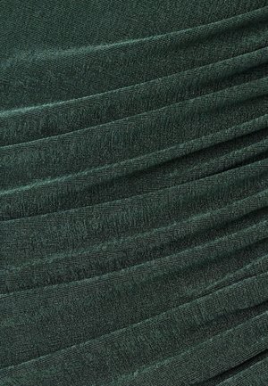 Tume roheline kangas tekstuurse koega, millel on diagonaalsed voldid ja peen läige. Materjal tundub pehme ja langeb sujuvalt.