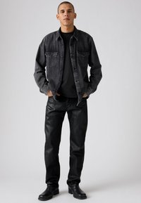 Camisa de mezclilla negra con bolsillos frontales, combinada con pantalones negros y botas negras. Textura suave y ajuste entallado. Diseño sencillo, sin patrones.