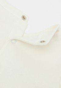 Helles cremefarbenes Kleidungsstück mit gerippter Textur. Verfügt über einen Druckknopfverschluss am Kragen und ein weiches Material für Komfort.