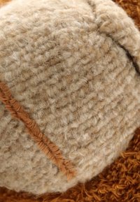 Gros plan d'un tissu en laine texturée couleur crème avec une couture marron cousue en diagonale.