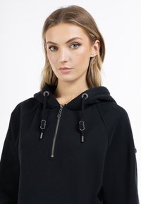 Felpa nera con zip realizzata in tessuto morbido. Dotata di cappuccio, cordoncino con puntali metallici e zip frontale. Texture liscia e design aderente.
