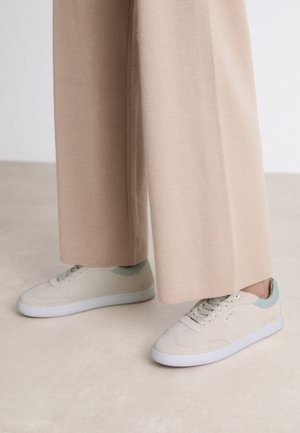 Beige sneakers met lichte groene accenten, gemaakt van zacht materiaal, met een klassiek ontwerp, ronde neus en witte rubberen zolen.