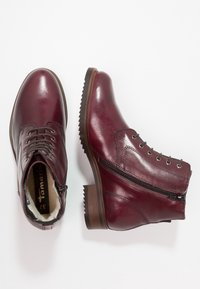 Bordowe skórzane botki za kostkę o fakturowanym wykończeniu, z przodem na sznurowanie, bocznym zamkiem błyskawicznym oraz kontrastującą brązową podeszwą gumową z ząbkowanymi brzegami.