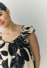 Voľná béžová blúzka s čiernym kvetinovým vzorom. Má volánové rukávy a výstrih do tvaru srdca. Vyrobená z ľahkého materiálu.