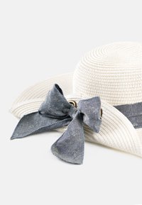 Szeroka słomiana czapka w kolorze białym z akcentem w postaci denimu w kształcie kokardy. Kokarda ma subtelny wzór w kotwice, co dodaje szczegółu do projektu.
