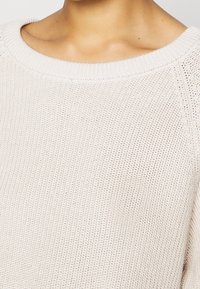Pull beige clair en maille avec une coupe décontractée. Caractéristiques d'un large décolleté et d'un tissu texturé avec un motif de maille lâche.