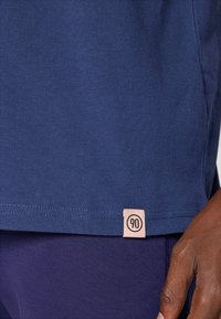 Marineblå bomulds T-shirt med lige snit. Har et lille pink mærke med "90" i kanten. Glat tekstur, korte ærmer.