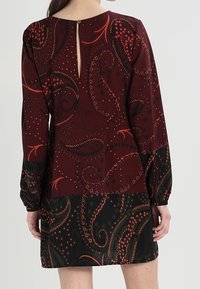Abito paisley bordeaux con maniche lunghe, presenta una schiena a chiave e una sezione inferiore nera a contrasto, che mette in mostra intricati motivi e texture.