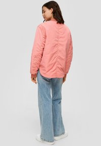 Chaqueta bomber rosa con puños y dobladillo acanalados, textura acolchada y un acabado suave. Usada sobre unos pantalones de mezclilla de pierna ancha en azul claro.