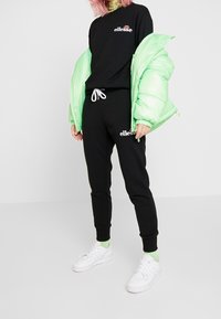 Svart sweatshirt med logotyp, svarta joggers med dragsko, mintgrön pufferjacka och vita sneakers med gröna strumpor. Slät textur.