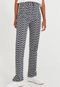 Pantalones de rayas en azul marino y blanco con un diseño ondulado, con cintura ajustada y bolsillos laterales. Combinados con zapatillas deportivas blancas.