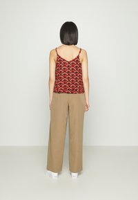 Camisola de padrão vermelho com alças finas, combinada com calças largas bege e ténis brancos, vista de costas contra um fundo neutro.