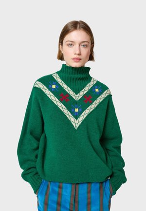 Grüner Wollpullover mit hohem Kragen, der ein cremefarbenes geometrisches Muster und bunte Blumenstickerei aufweist. Überschnittene Passform mit gerippten Bündchen.