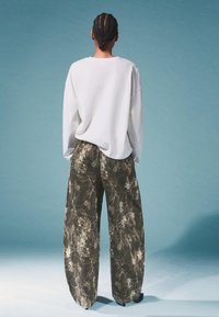 Biała, oversize koszula z długimi rękawami w zestawie z luźnymi, wzorzystymi oliwkowymi spodniami o marmurkowej strukturze i szerokich nogawkach.