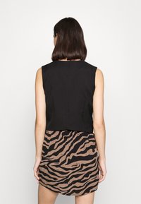 Schwarzes ärmelloses Top mit einem verkürzten Design, kombiniert mit einem braunen Rock mit einem schwarzen Zebra-Streifen-Muster. Glatte Stofftextur.
