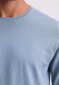 Himmelblaues, langärmliges Rundhals-Sweatshirt mit subtiler Textur und einem geprägten "M OP"-Logo auf der Brust. Aus weichem Stoff gefertigt.