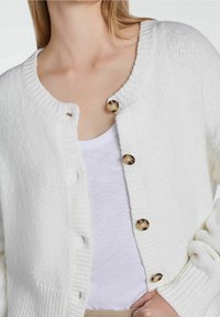 Vit stickad cardigan med en texturerad finish, ribbad krage och muddar, med stora gyllene knappar framtill.