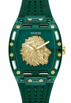 Une montre verte transparente présente une tête de lion dorée sur le cadran, des accents dorés et un bracelet en caoutchouc vert doux avec un motif texturé.