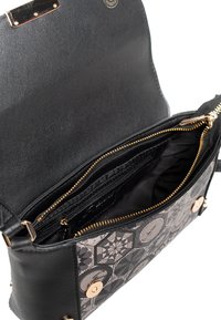 Černá kožená taška s přední stranou z látky s vzorem. Má zapínání na zip, zlaté kovové doplňky a několik vnitřních přihrádek.