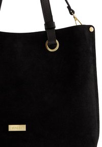 Sort suede håndtaske med en glat tekstur, detaljer i guldfarvet hardware og et mærkeplade. Har en skulderrem og metalringdetalje.