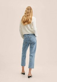 Jean en denim bleu clair avec broderie florale, coupe droite courte, taille haute et design de poche arrière, accompagnés d'un pull blanc.