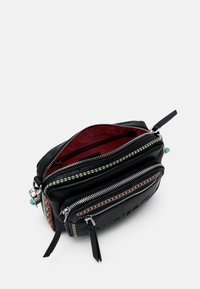 Musta nahkalaukku, jossa useita vetoketjutaskuja, värikkäillä ompeleilla ja punaisella vuorauksella. Varustettu metallikoristeilla.