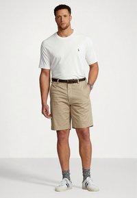 Balta T-krekls ar apaļu apkakli, haki šorti ar jostu, pelēkas zeķes, baltas sporta apavi. Ikdienišķs apģērbs, vienkrāsaini toņi, brīvs piegriezums.