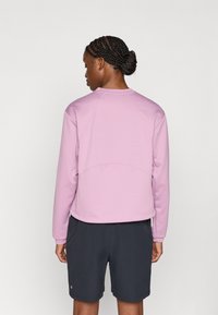 Ροζ ανοιχτό, υφασμάτινο φούτερ με μακριά μανίκια, σχέδιο ράγκλαν και στρογγυλή λαιμόκοψη, συνδυασμένο με σκούρο σορτς, εμφάνιση από πίσω.