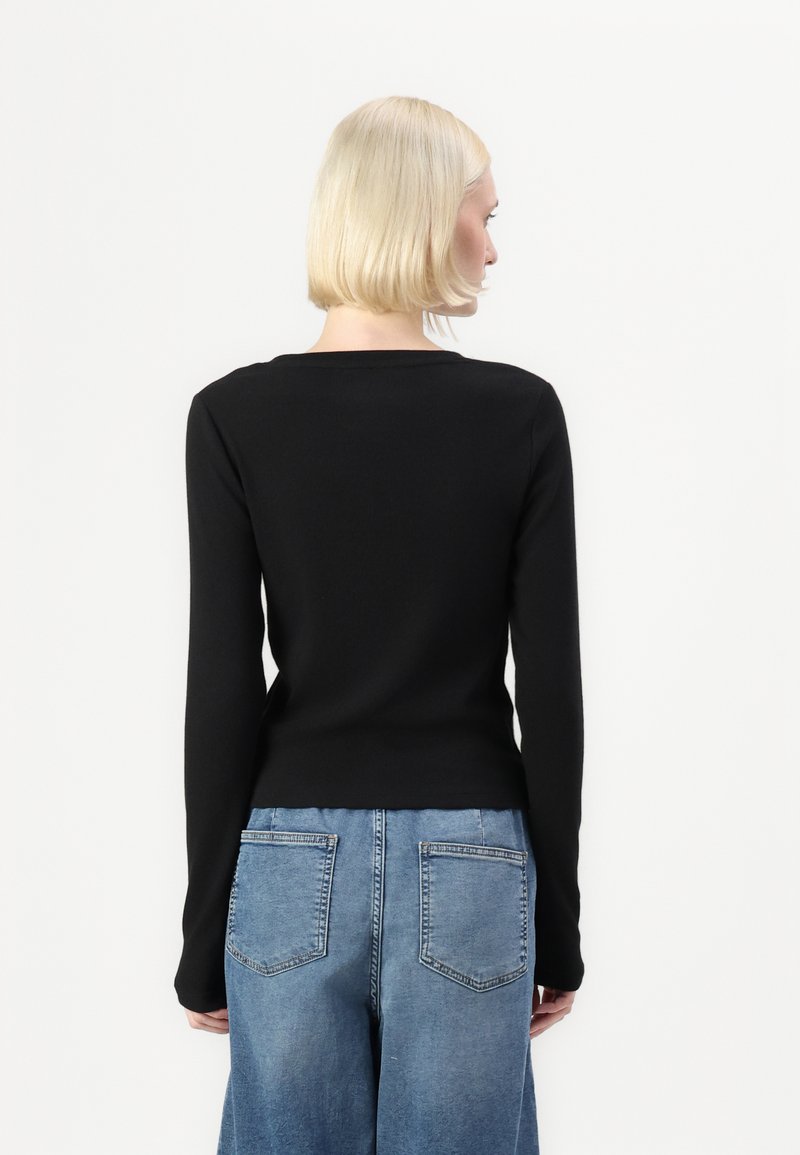 Top nero a maniche lunghe con design aderente e scollatura tonda, abbinato a jeans a gamba larga blu con tasche posteriori. Semplice e senza cuciture.