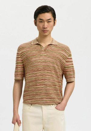 Ung mand med kort hår iført en tekstureret, stribet polo-shirt i beige, brune og pink toner, og han holder en bog i sin venstre hånd.