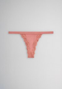 Pink lace-trimmed thong underwear laid flat on a gray surface, showing a narrow waistband and floral lace detailing on the edges.