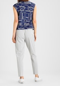 Navy patterned sleeveless top with abstract white designs, paired with light gray tapered pants and white sneakers.