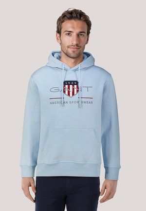 Felpa leggera blu chiaro realizzata in misto cotone, con tasca a marsupio frontale, cappuccio con coulisse e logo ricamato con accenti rossi e blu navy.