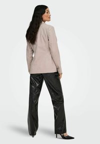 Jasnoszara, dopasowana marynarka o kroju na miarę, zestawiona z czarnymi, błyszczącymi spodniami z wysokim stanem oraz czarnymi szpilkami z ostrym noskiem.