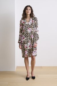Leopardmönstrad klänning med rosa och vita blommiga detaljer; långa ärmar, V-ringning, lös passform, knälång, bärs med svarta spetsiga skor.