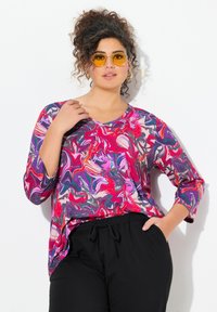 Kleurige, lange mouw top met een zwirlend gemarmerd patroon in roze, paars en oranje. V-hals ontwerp. Zwarte broek met een relaxte pasvorm.