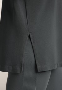 Top atletiecher negru cu fanta pe lateral, realizat dintr-un material moale, asortat cu colanți texturați gri închis. Accent pe linii curate și un design minimalist.