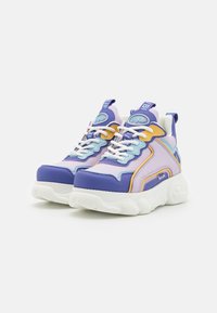 Tenis multicoloridos com materiais sintéticos em roxo, lavanda e amarelo, uma sola branca robusta e costuras detalhadas com acentos em contraste.