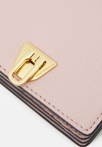 Portafoglio in pelle rosa chiaro con superficie texture, caratterizzato da una chiusura triangolare in tonalità oro con dettagli del marchio. I bordi sono finiti in modo scuro.