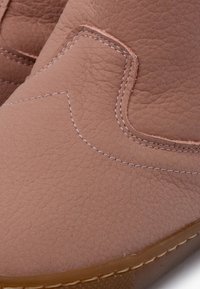 Brun lædersko med slip-on design, struktureret finish, syninger og fleksibel gummisål. Kontrastsyning langs sømmene.