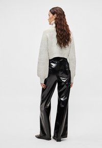 Camisola cinza clara curta com malha texturada, combinada com calças pretas de vinil de cintura alta, com acabamento brilhante e pernas largas.